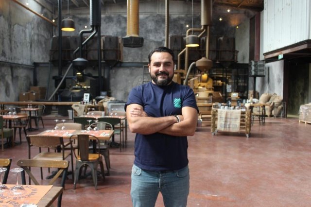 SOKAK KÜLTÜRÜYLE BU İŞLERİ ÖĞRENDİK
“Bizim derdimiz sokak. Biz öğrendiğimiz her şeyi sokakta öğrendik. Mekanlarımızda da sokağı yansıtmaya çalışıyoruz. Biz o doğallıktan ve sokak kültüründen kopmak istemiyoruz. Avm’ye girmeme sebeplerimizden birisi de mutlu yatırımcılar istiyoruz. Avm’lerde bunu sağlamak biraz zor. Yüksek maliyetlerin olmadığı bir avm olursa oraya da şube verebiliriz. Doğru şartlarda doğru maliyetlerle olursa avm’lerde de yeni şubelerimiz yer alabilir.”
PABLO ARTİSAN BACKSTAGE HAYRAN BIRAKIYOR
Pablo Artisan Backstage İzmir Gaziemir Sarnıçta yer alıyor. Burayı bizim Almanya’da gezerken gördüğümüz en etkilendiğimiz kahve kavurma hangarına benzetmeye çalıştık. Bu kadar büyük bir hangar bulacaksın, içerisine makineleri koyacaksın, eğitimleri orada yapacaksın. Bizim için hayaldi. Tamamen hayalimizdeki konsept buydu. Bu hangarlardan Türkiye’de tek yer burası. Dünya’da bu şekilde en fazla 10 mekan vardır.  Yemek etkinlikleri yapıyoruz. Hamburger, makarna, et çeşitleri var. Çölde vaha gibi bir yer yaptık. Giren herkes önce bir şaşırıyor. Burası Türkiye’nin en büyük metrekare olarak kavurma fabrikası. Kapasite anlamında ilk beşe girer.”